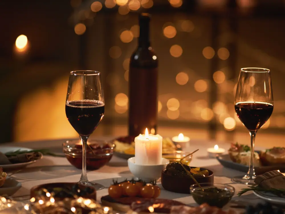 Mesa à luz de velas com duas taças de vinho tinto e petiscos